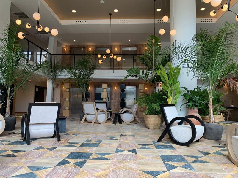 Nowoczesna, jasna lobby hotelowa z przeszklonymi balustradami, roślinami i unikalnymi meblami.