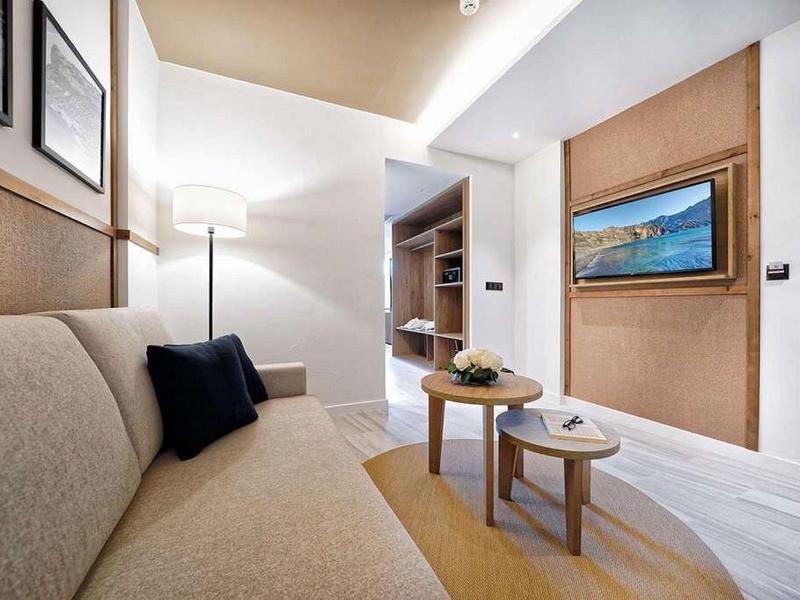 Nowoczesny pokój hotelowy z sofą, stolikami kawowymi i telewizorem na ścianie.