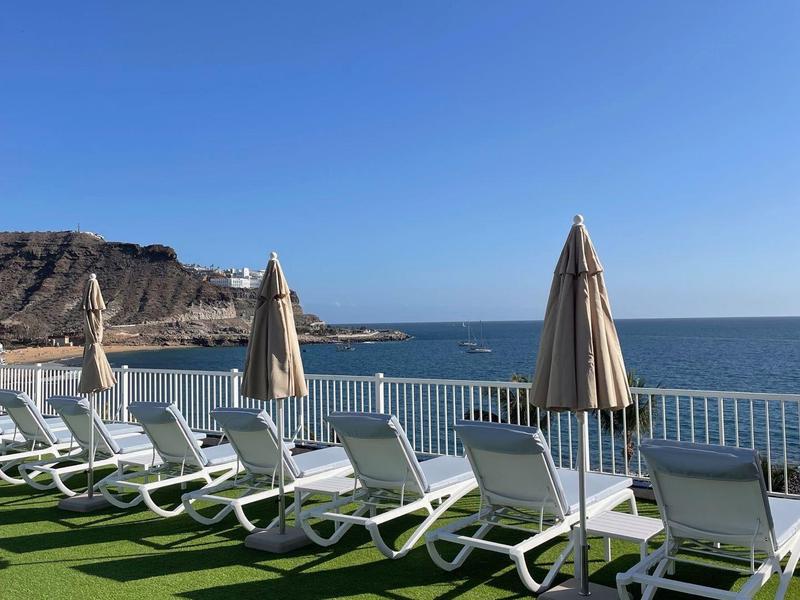 Rzędy leżaków i parasoli na tarasie z widokiem na morze i górę.