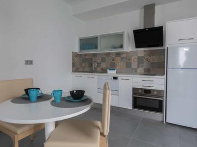 Modern kitchenette with white cabinets, colorful tiled backsplash, and small dining area.