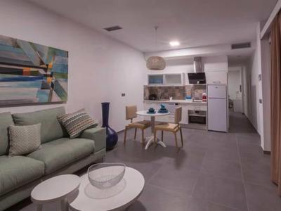 Modern living area with gray sofa, dining table, and open kitchen in neutral tones.
