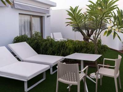 Modern outdoor seating area with white loungers, chairs, and table on green grass by a white wall.