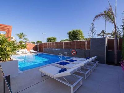 Modern outdoor pool with sun loungers and umbrellas under a clear blue sky.