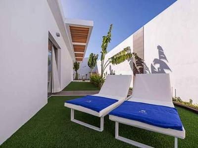 Two white lounge chairs with blue cushions on green grass beside white walls under a blue sky.