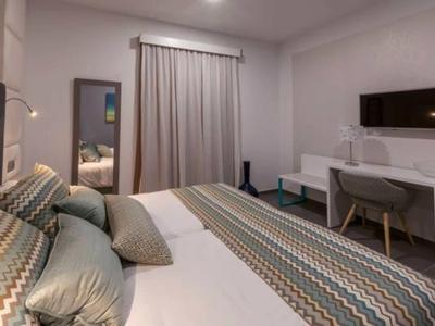 Modern hotel room with large bed, desk, chair, and flat-screen TV.