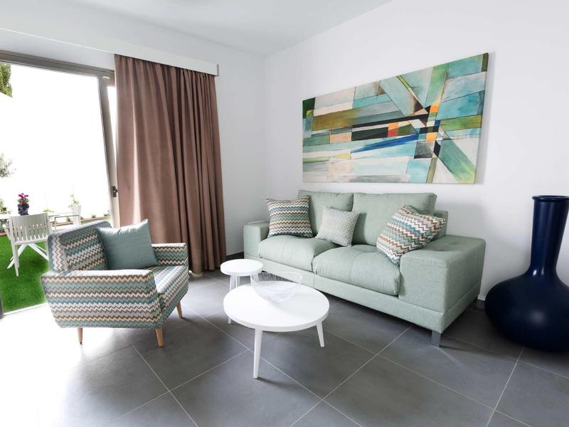 Modern living room with sofa, armchair, coffee table, and view of a terrace.