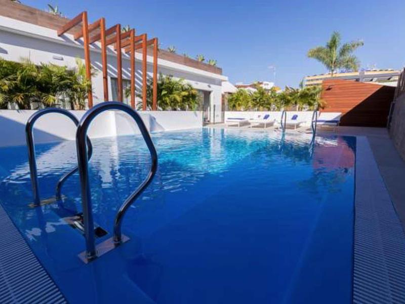 Modern pool with tall ladder, surrounded by white tiled floor and buildings in the background.