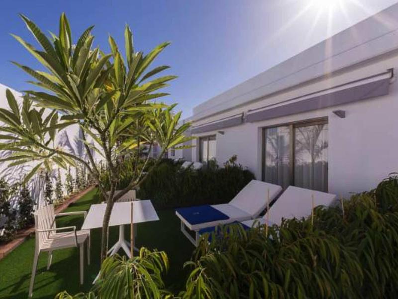 Terrace with sun loungers, table and chairs, surrounded by plants under clear sky.