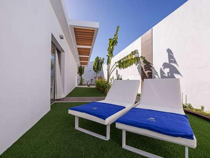 Two white lounge chairs with blue cushions on green grass beside white walls under a blue sky.