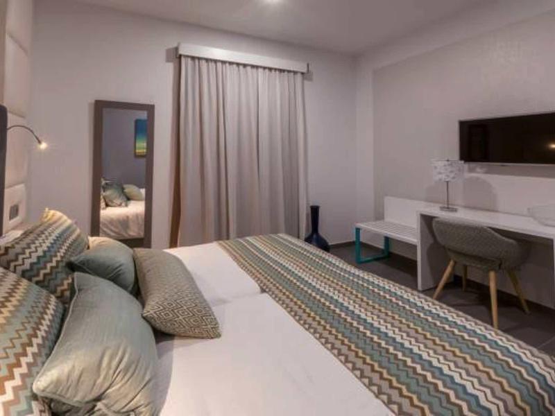 Modern hotel room with large bed, desk, chair, and flat-screen TV.