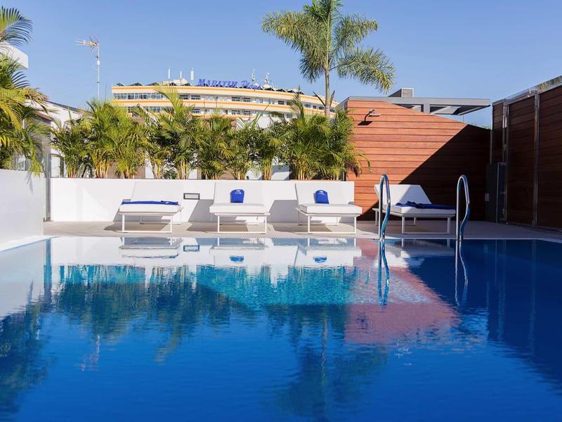 Clear pool area with sun loungers and palm trees in a sunny hotel setting.