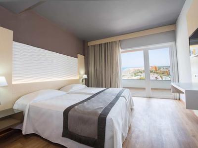 Helles Hotelzimmer mit Doppelbett, großem Fenster, hellen Wänden und Holzboden.