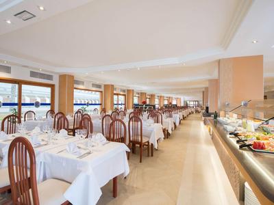 Großer, heller Speisesaal mit vielen Tischen, weißen Tischdecken und Holzstühlen, Buffet rechts.