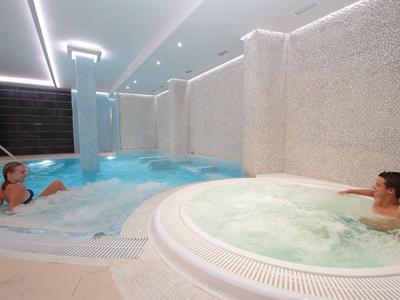 Innen-Poolbereich mit zwei Personen im Whirlpool und Schwimmbecken, Wände in hellen Tönen.