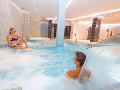 Zwei Personen entspannen in einem großen, modernen Whirlpool mit Wasserfall und sanfter Beleuchtung.