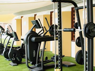 Fitnessraum mit verschiedenen Trainingsgeräten, darunter Laufband, Fahrrad und Gewichtsstation.
