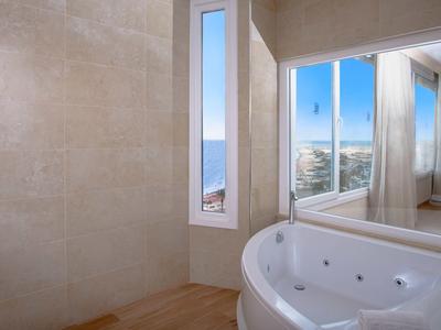 Helles Badezimmer mit eckiger Badewanne, Holzfußboden, beige Fliesen und großem Spiegel.