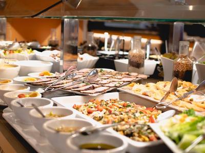 Buffet mit verschiedenen Salaten, Dressings und kalt zubereiteten Speisen auf weißen Tellern.