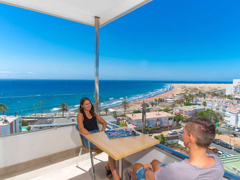 Dwie osoby siedzą na balkonie z widokiem na morze i nadmorskie miasto.