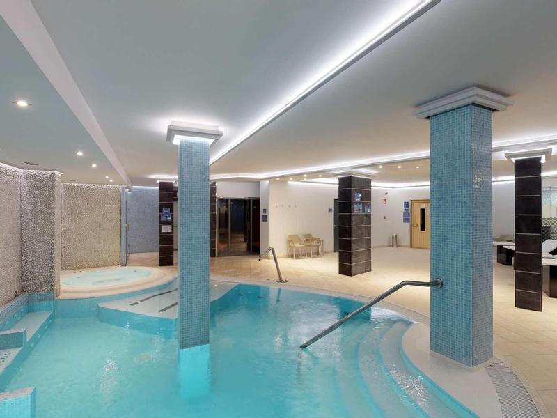 Nowoczesna strefa wellness z krytym basenem, kolumnami i relaksującymi leżakami.