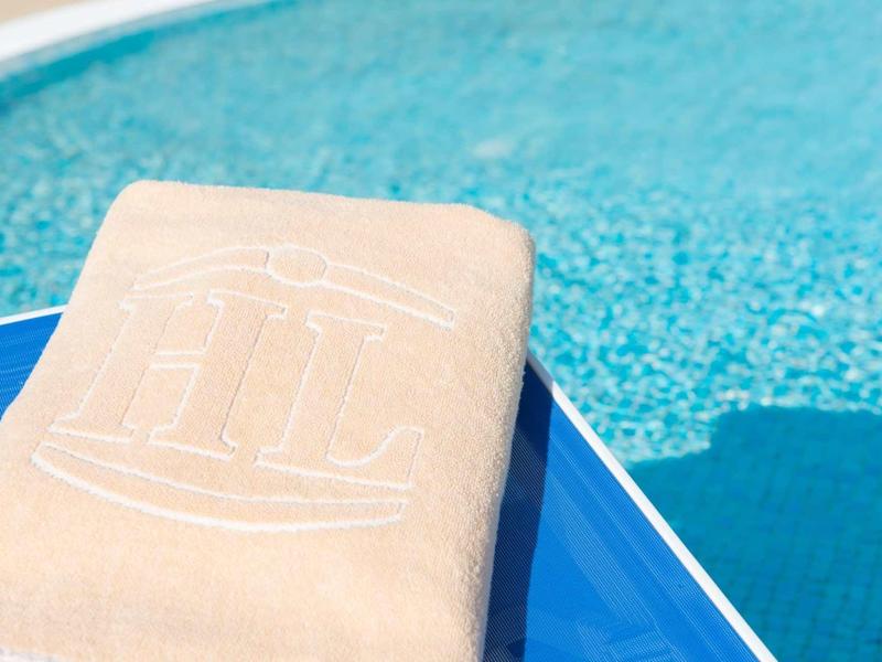 Widok na beżowy ręcznik na niebieskim leżaku przy basenie z czystą wodą.