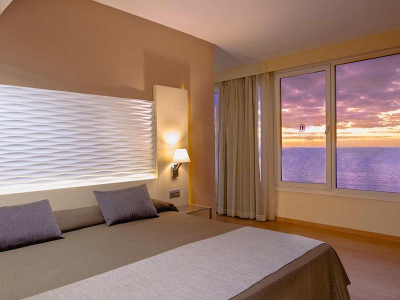 Nowoczesny pokój hotelowy z dużym oknem i widokiem na morze o zachodzie słońca.