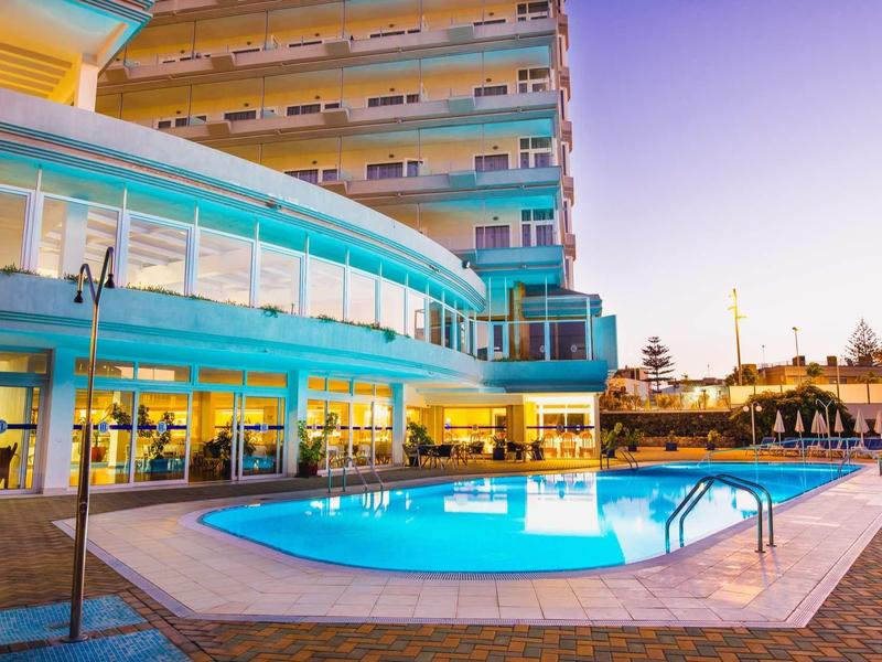 Nowoczesny hotel z basenem na zewnątrz i tarasem o zachodzie słońca.