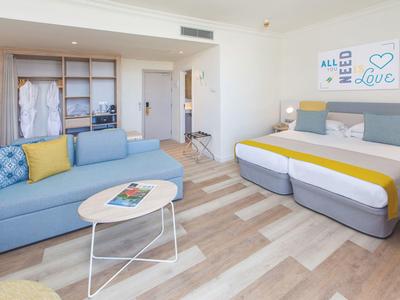 Helles Hotelzimmer mit Doppelbett, blauem Sofa, rundem Tisch und Holzfußboden.