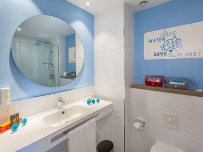 Helles Badezimmer mit großem rundem Spiegel, weißer Waschtisch und blauen Wänden, moderne Dusche sichtbar.
