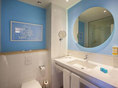 Modernes Badezimmer mit blauem Spiegel, weißem Waschbecken und blauem Wandbild über der Toilette.