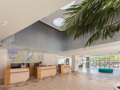 Große helle Lobby mit drei Rezeptionstresen, Palmen und heller Marmoroptik auf dem Boden.