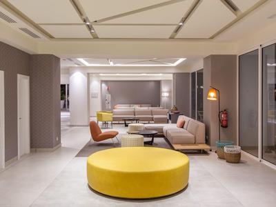 Moderner Wohnraum mit gelbem Sitzpouf, beige Sofas, braunem Sessel und großer Glasfront.
