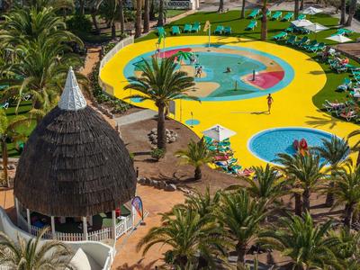 Bunte Schwimmbecken mit mehreren Rundungen, umgeben von Palmen und Sonnenschirmen in tropischer Anlage.
