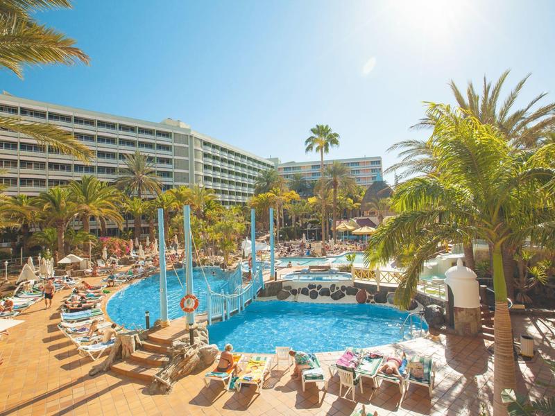 Sunny hotel resort with pool, lounge chairs, and palm trees under clear sky.