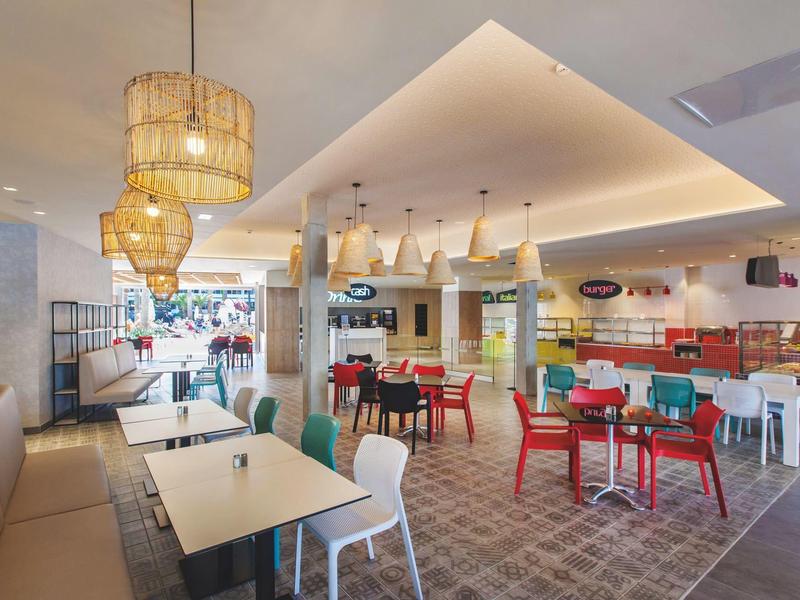 Bright modern hotel restaurant with colorful chairs and wooden pendant lamps.