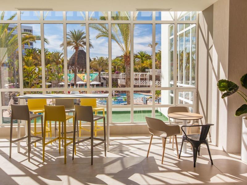Bright hotel lounge area with large windows, palm view, and modern seating arrangement.