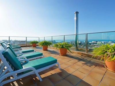 Rooftop terrace with sun loungers, potted plants, and sea view under clear sky