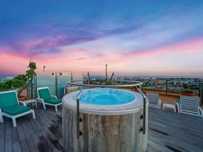 Round outdoor hot tub on a rooftop terrace with lounge chairs and sunset view.
