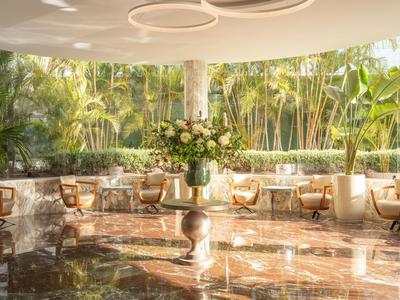 Helle Hotellobby mit Marmorfußboden, Blumenarrangement und Sitzbereichen mit Stühlen.
