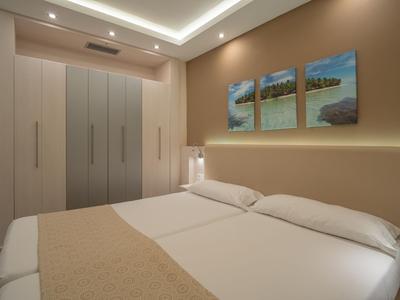 Modernes Hotelzimmer mit zwei Einzelbetten, beige Akzenten und Landschaftsbildern an der Wand.