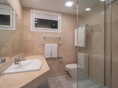 Hell gestaltetes Hotelbadezimmer mit Waschtisch, Toilette und Dusche mit Glasabtrennung.
