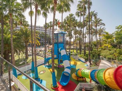 Bunte Wasserrutsche und Spielplatz in einem tropischen Resort mit Palmen bei Sonnenschein.