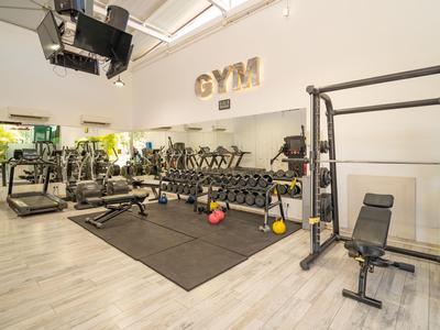 Helles Fitnessstudio mit Gewichten, Laufbändern und Kraftgeräten auf Holzboden.