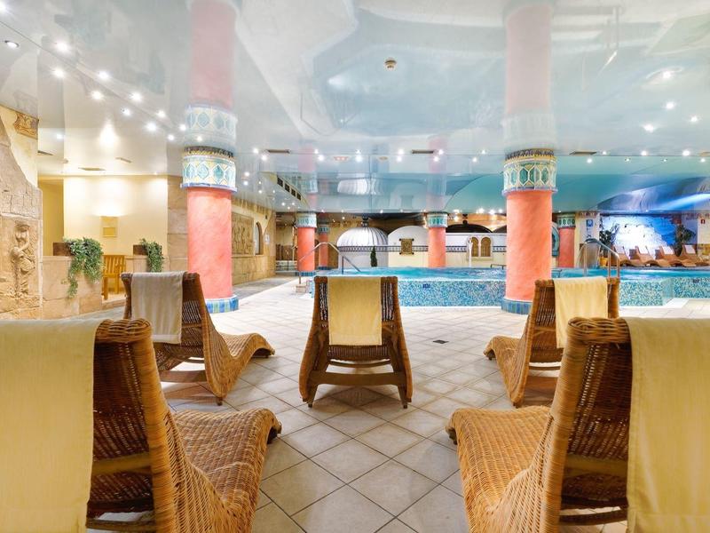 Piscina interna con sedie in rattan e illuminazione calda in un ambiente alberghiero.