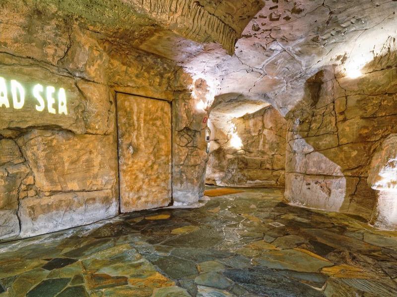 Interno di una grotta artificiale con pareti di pietra e scritta luminosa 'Dead Sea'.