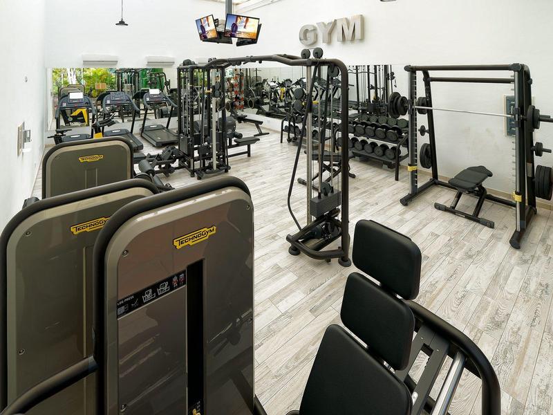 Palestra con attrezzature e pesi, pavimento chiaro in legno e pareti bianche.