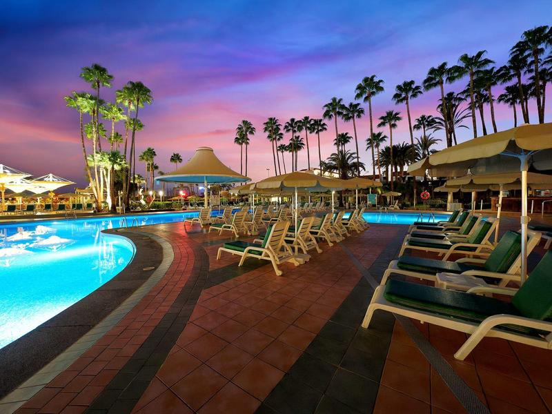 Piscina illuminata al tramonto con lettini e palme in un hotel tropicale.