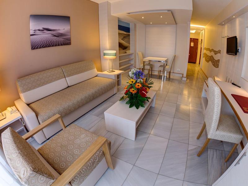 Soggiorno d'hotel moderno con divano, poltrona, tavolino e decorazioni floreali.