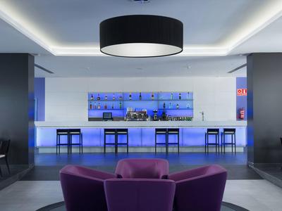 Moderne Bar mit blauer LED-Beleuchtung, schwarzen Stühlen und violetten Sesseln im Vordergrund.