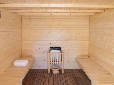 Innenraum einer Holzsauna mit zwei Holzbänken, einem Saunaofen und einem Holzeimer mit Schöpfkelle.
